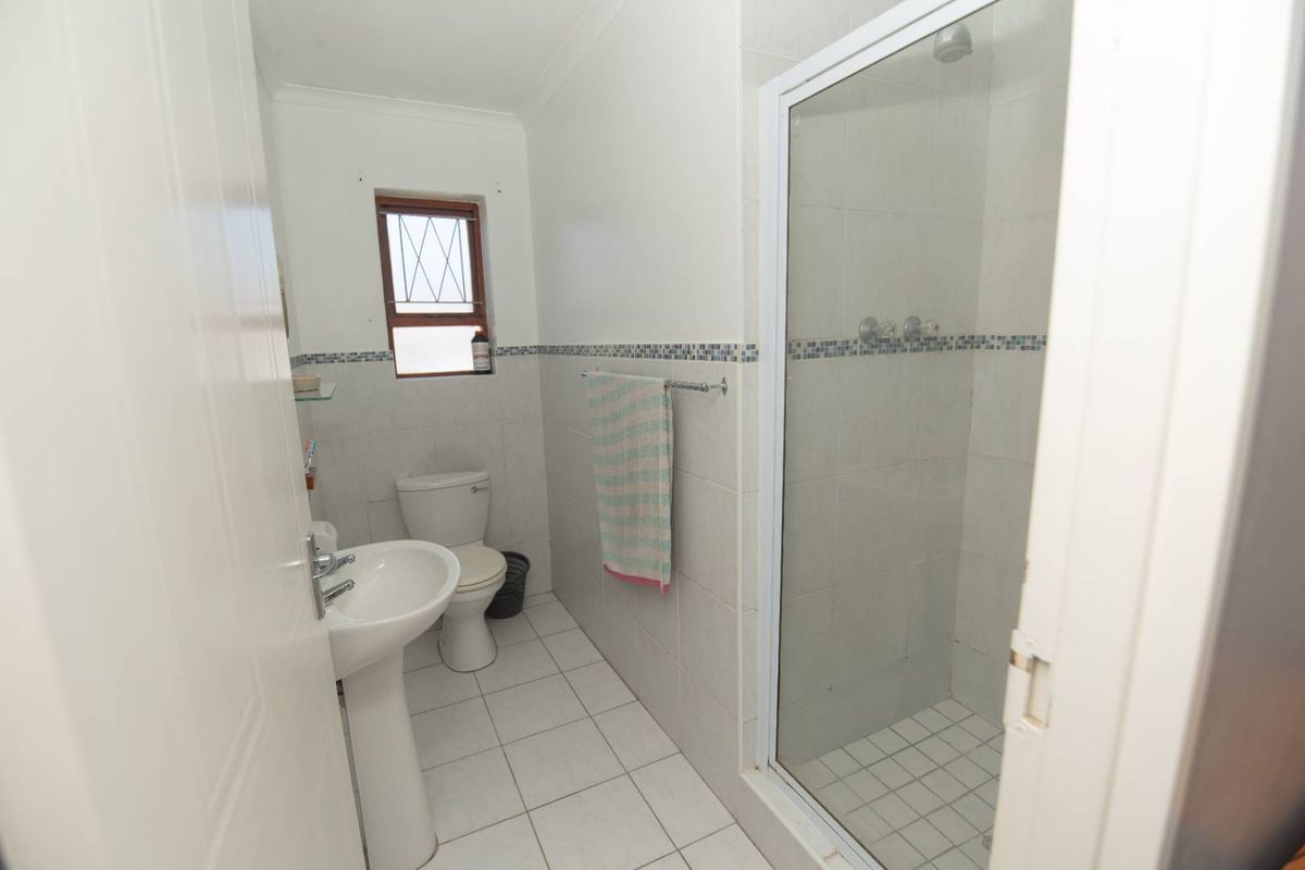 A functional bathroom featuring a pedestal basin, a standard toilet, and a glass-enclosed shower with tiled walls and flooring.