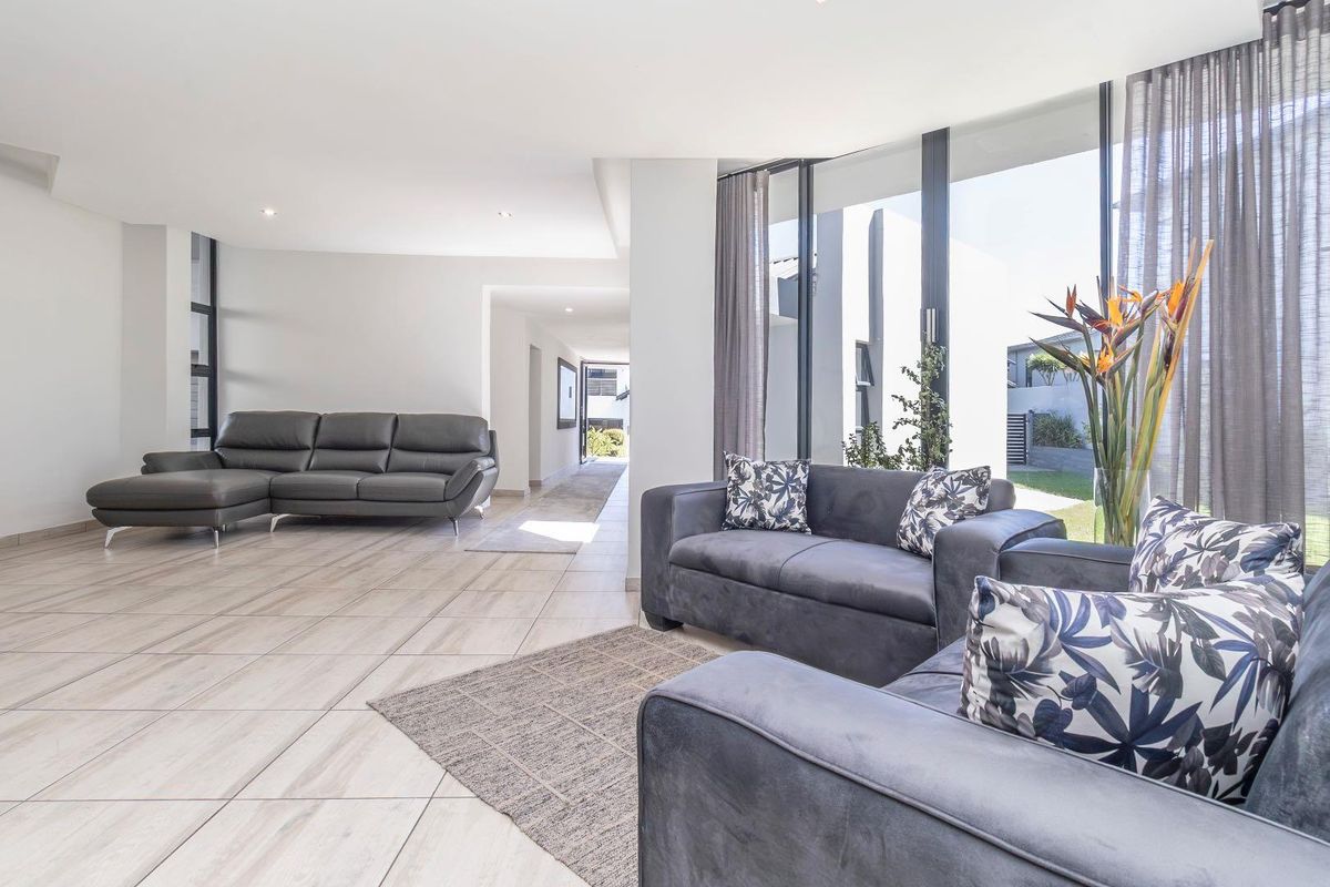 Spacious open-plan living area featuring large floor-to-ceiling windows, tiled flooring, and seamless access to the hallway and outdoor garden area.