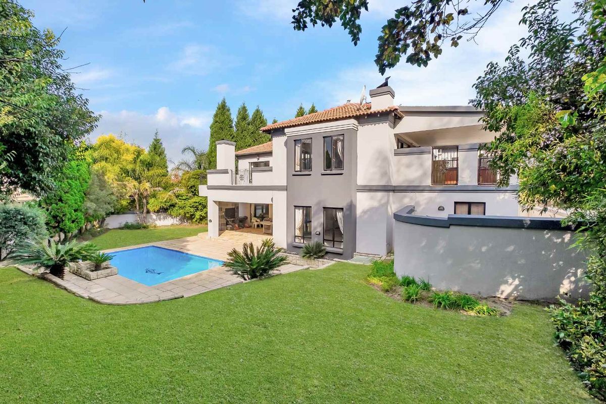 Rear view of a two-story house featuring a swimming pool, paved patio area, balcony, and a well-maintained garden.