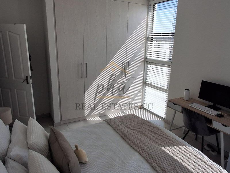 A well-lit bedroom featuring built-in cupboards, tiled flooring, and large windows with horizontal blinds, offering a clean and functional living space.