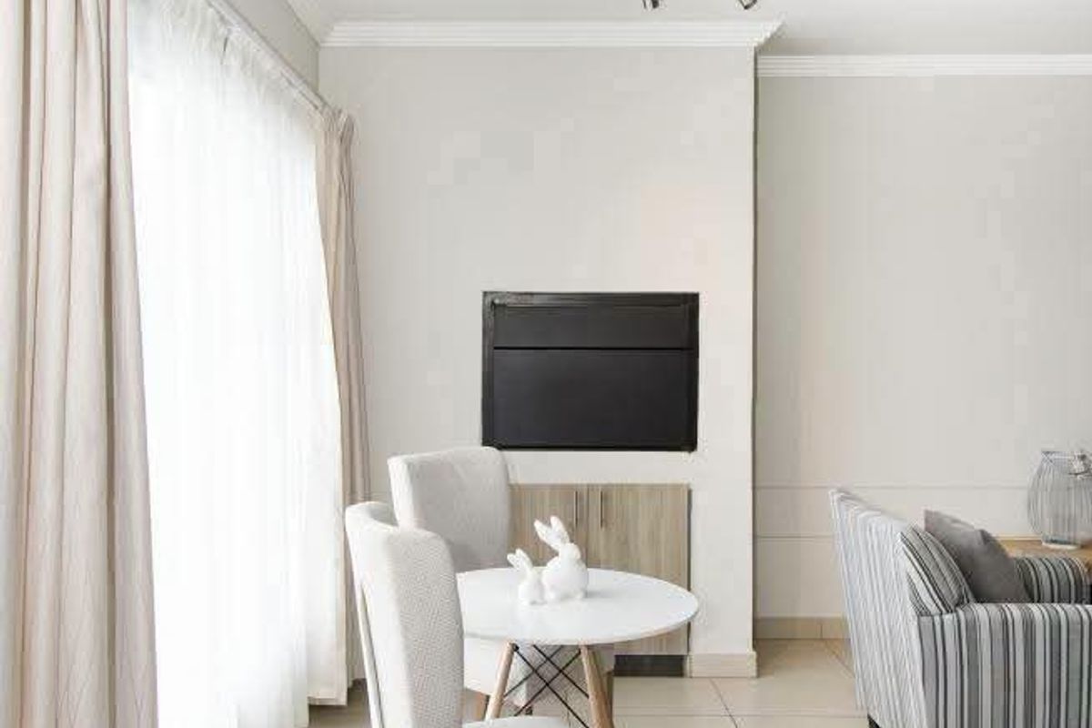 A bright living area featuring neutral tiled flooring, crown molding, and a built-in fireplace, offering a clean and well-maintained space.