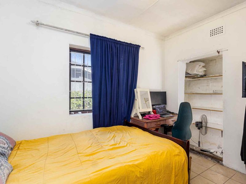 A bedroom featuring tiled flooring, a window with security bars, and a built-in shelving alcove requiring cosmetic updates.