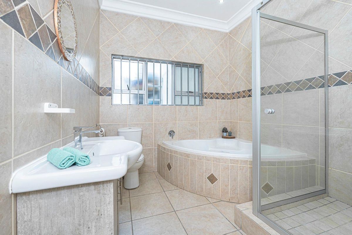 A tiled bathroom featuring a corner bathtub, a separate glass-enclosed shower, a pedestal basin, and a toilet with security bars on the window.