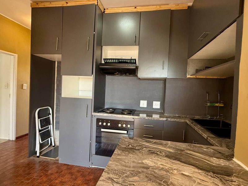 A compact kitchen featuring dark grey cabinetry, built-in oven and hob, and stone-look countertops, currently requiring minor finishing touches to complete the installation.
