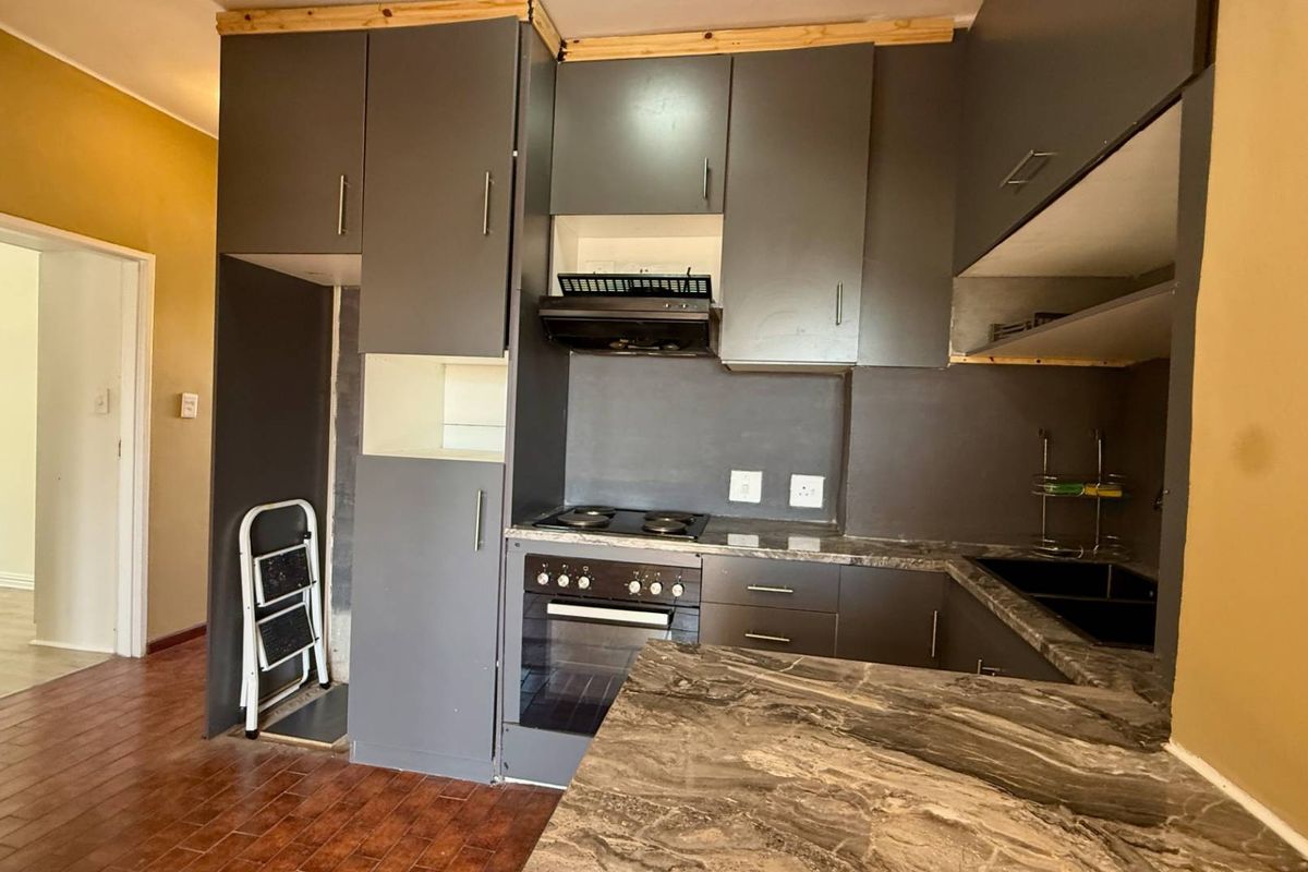 A compact kitchen featuring dark grey cabinetry, built-in oven and hob, and stone-look countertops, currently requiring minor finishing touches to complete the installation.