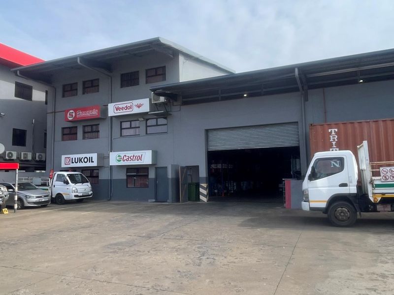 Front exterior view of a mixed-use industrial property featuring a large roller shutter door, concrete driveway, and multiple commercial signage panels.