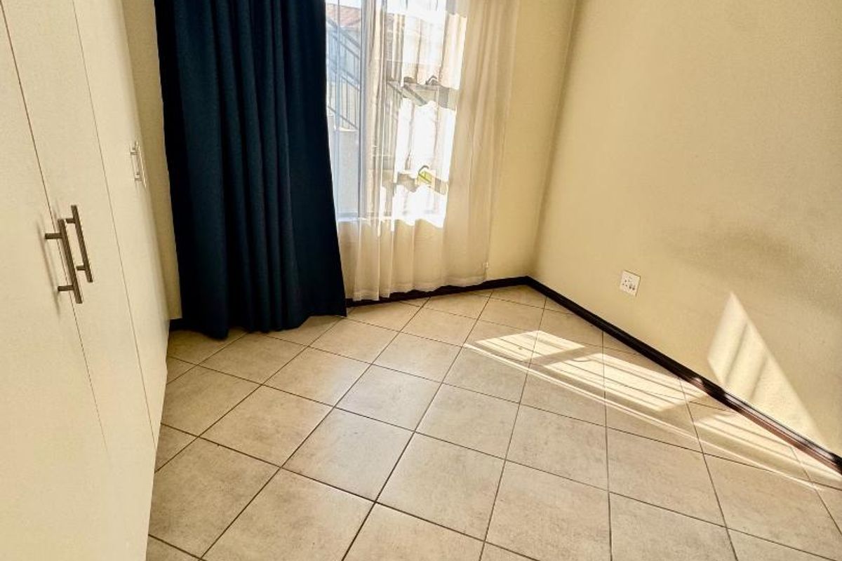 A bedroom featuring tiled flooring and built-in cupboards, offering a functional space with natural light.