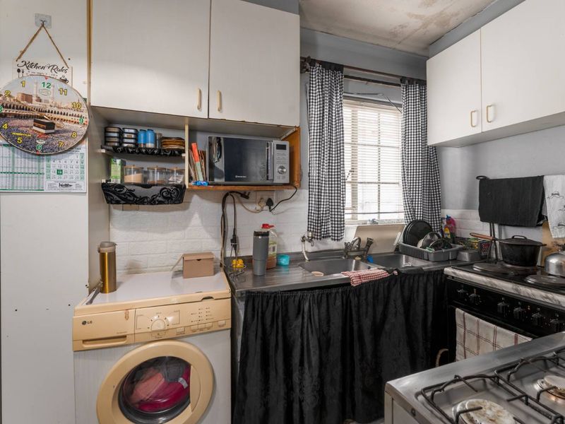 A compact kitchen featuring built-in cabinetry, a stainless steel sink, and a gas stove, requiring cosmetic updates to modernize the space.