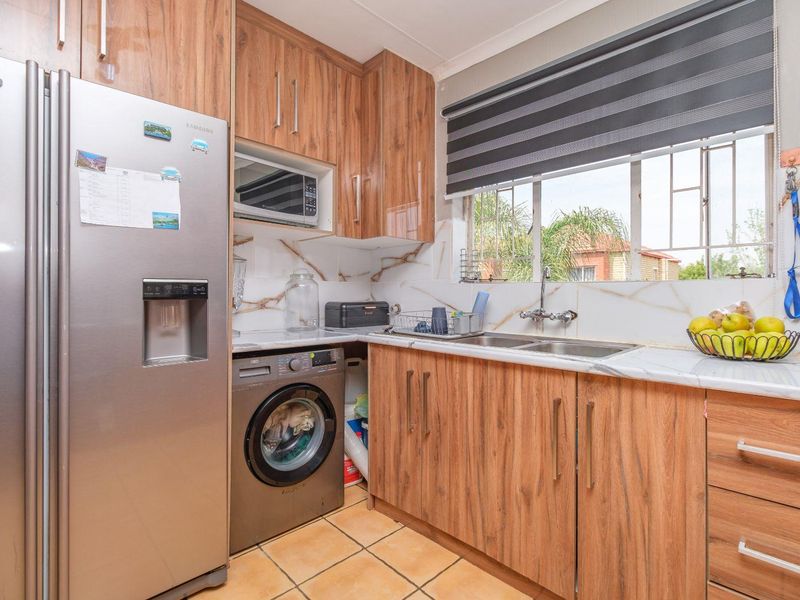 A functional kitchen featuring wood-grain cabinetry, marble-effect countertops, a double sink, and integrated microwave, complemented by tiled flooring and natural light.