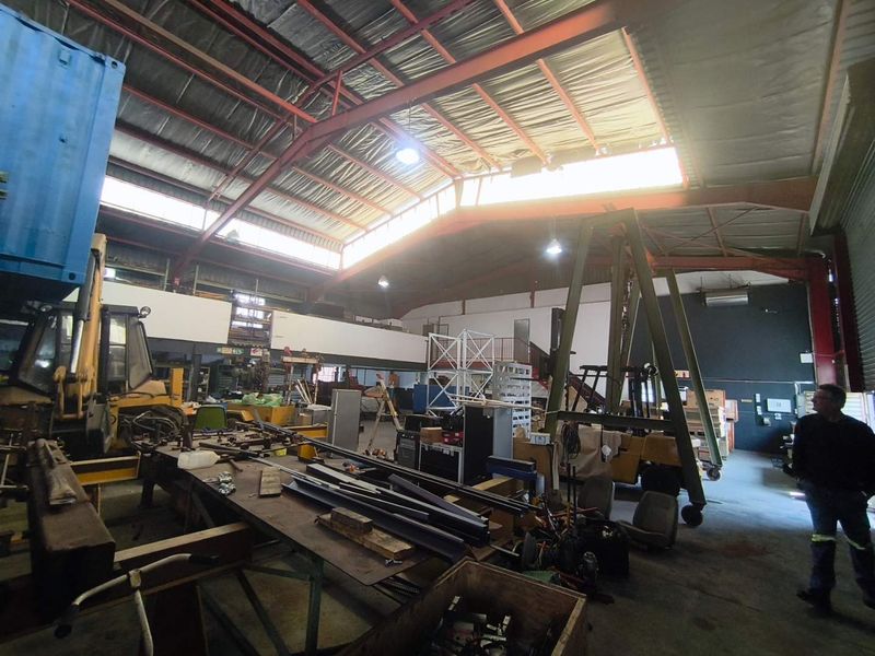 Spacious industrial warehouse featuring high-clearance ceilings with exposed steel trusses, mezzanine level, and concrete flooring, suitable for various commercial or storage operations.