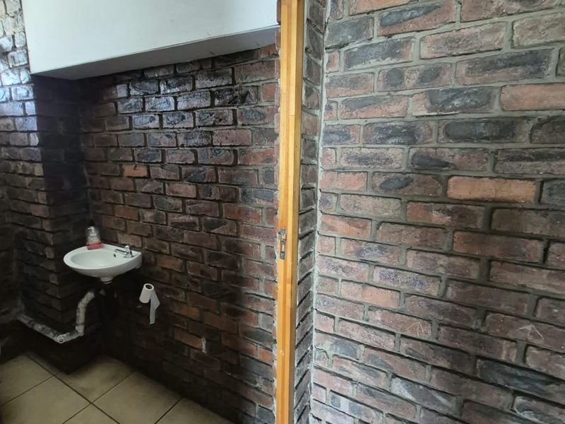 A small bathroom area featuring exposed brick walls, tiled flooring, and a wall-mounted basin, currently requiring renovation and finishing of structural elements.