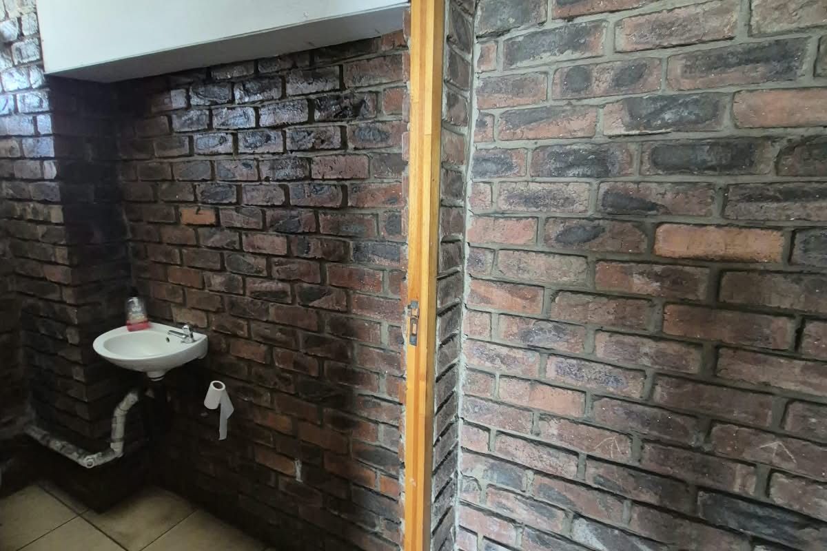 A small bathroom area featuring exposed brick walls, tiled flooring, and a wall-mounted basin, currently requiring renovation and finishing of structural elements.