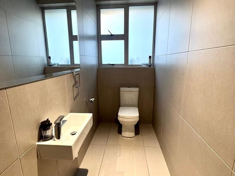 A modern, minimalist bathroom featuring neutral floor-to-ceiling tiling, a wall-mounted basin with chrome fixtures, and a toilet.