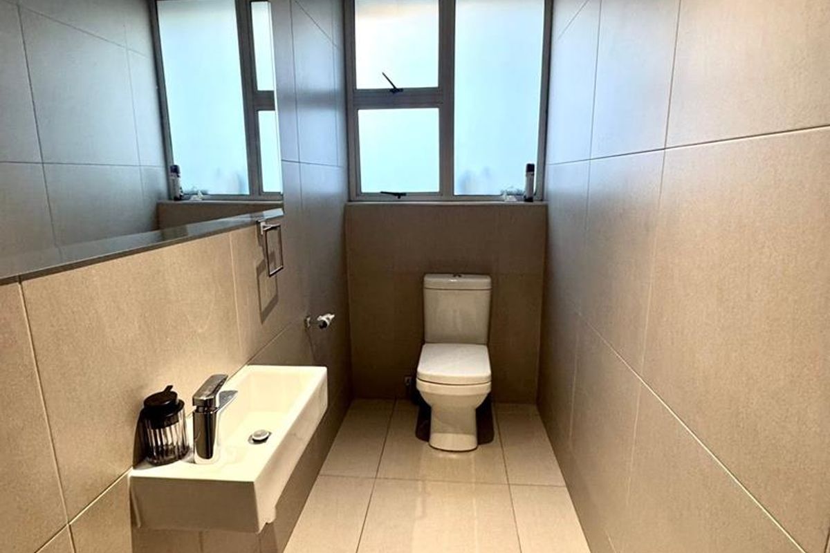 A modern, minimalist bathroom featuring neutral floor-to-ceiling tiling, a wall-mounted basin with chrome fixtures, and a toilet.