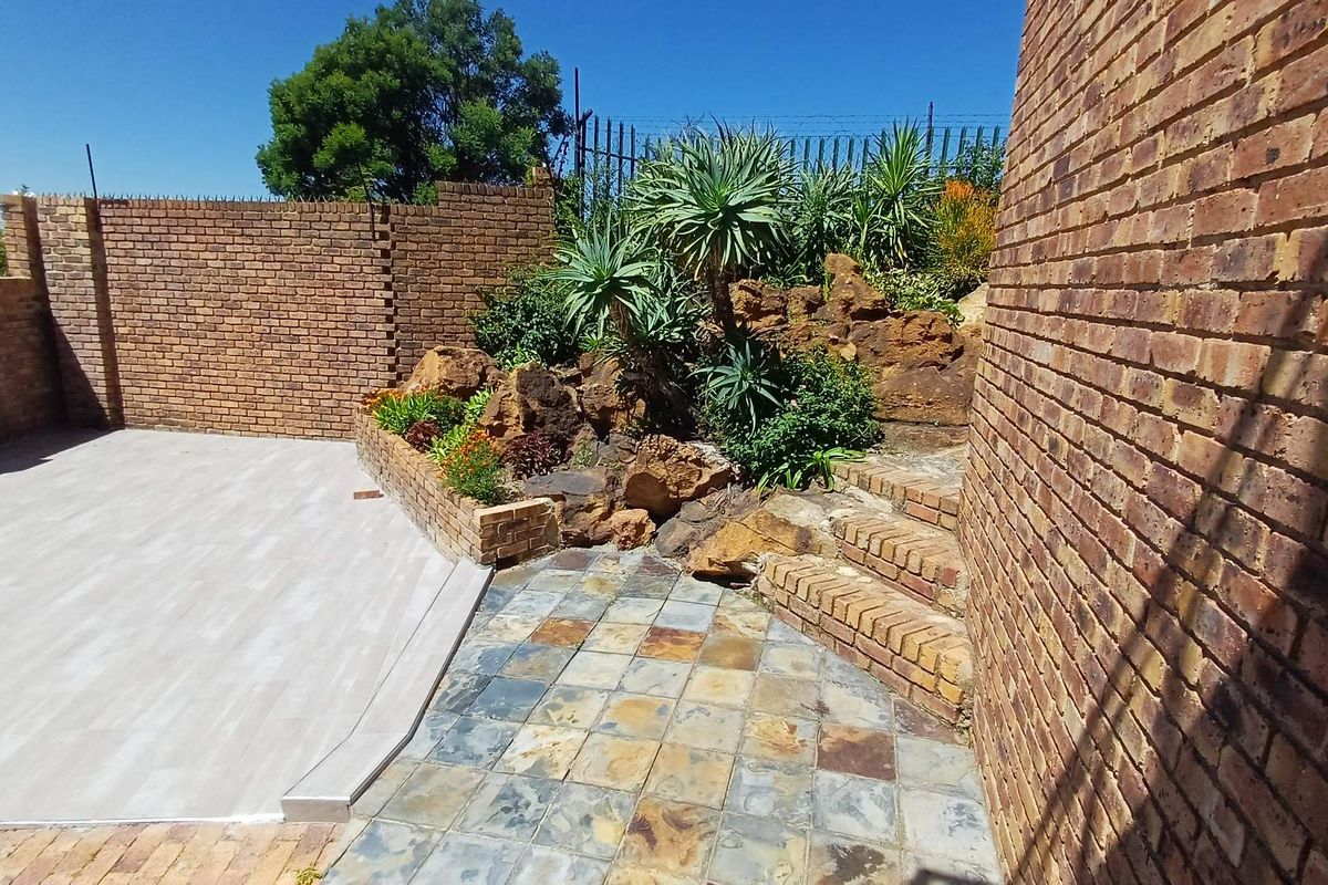 A private rear courtyard featuring a combination of paved and tiled surfaces, brick boundary walls, and a landscaped rockery with established plants.