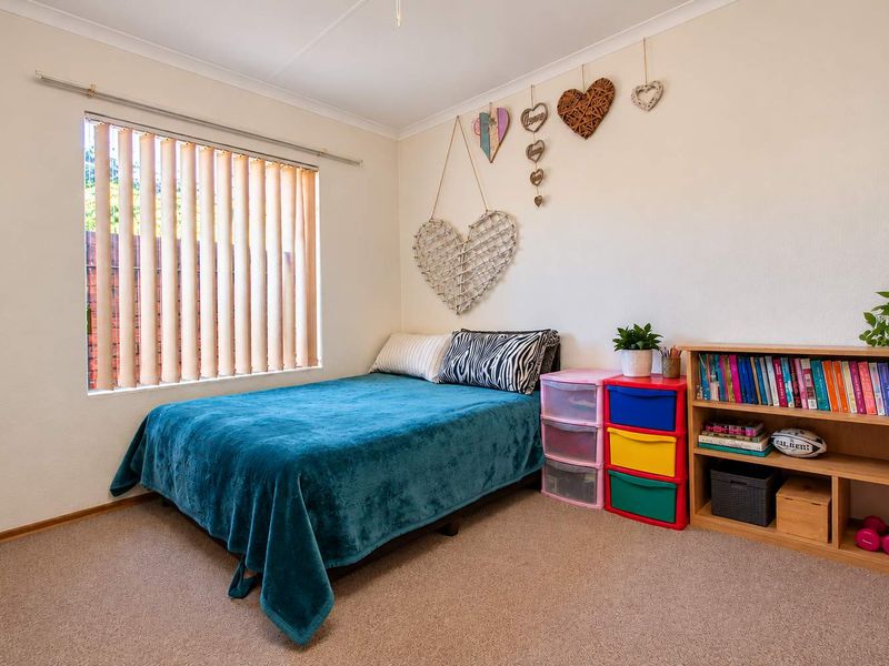 A functional bedroom featuring neutral walls, carpeted flooring, and a window fitted with vertical blinds.
