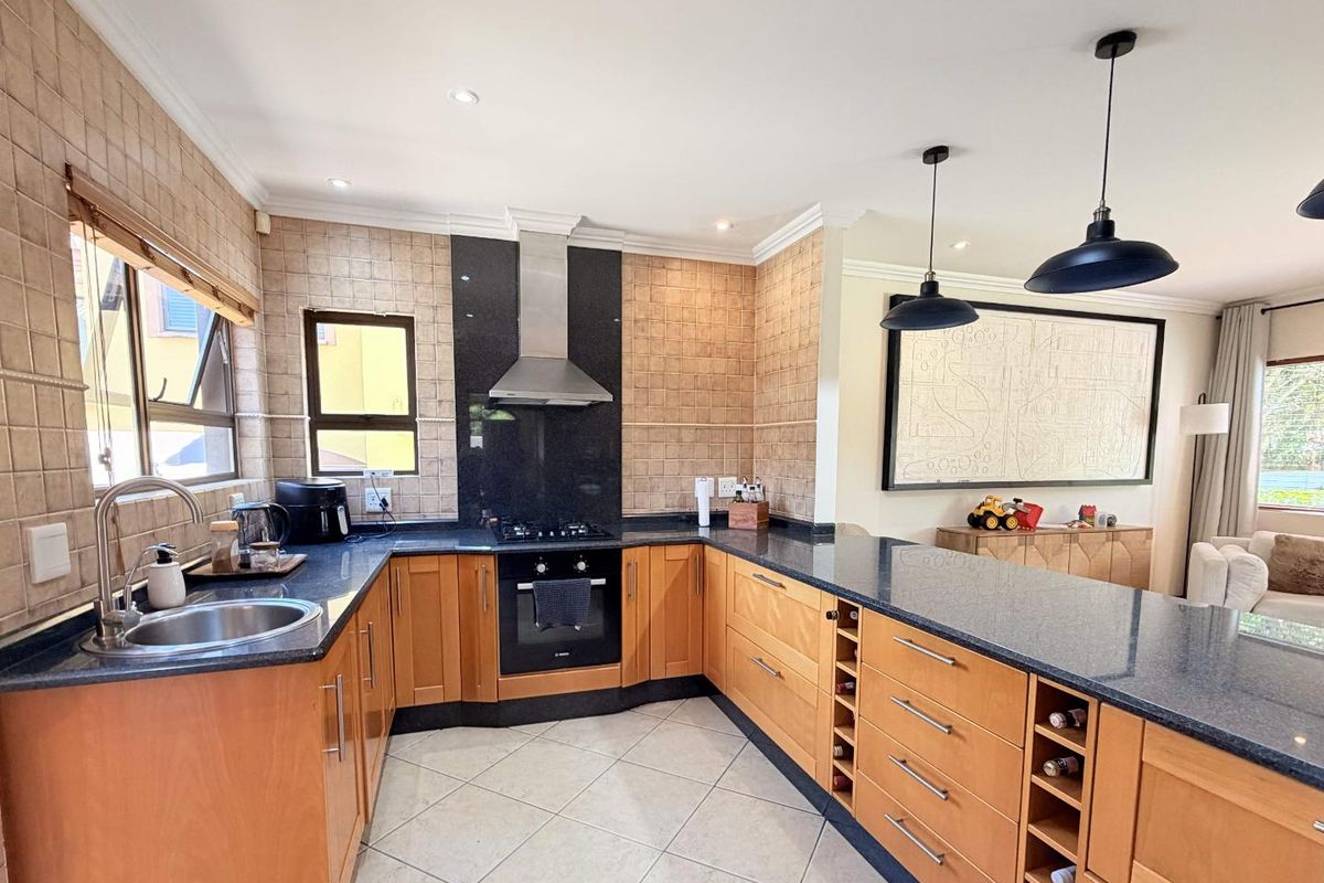A well-appointed kitchen featuring wooden cabinetry, granite countertops, a built-in oven with gas hob, and a breakfast bar island with integrated wine storage.