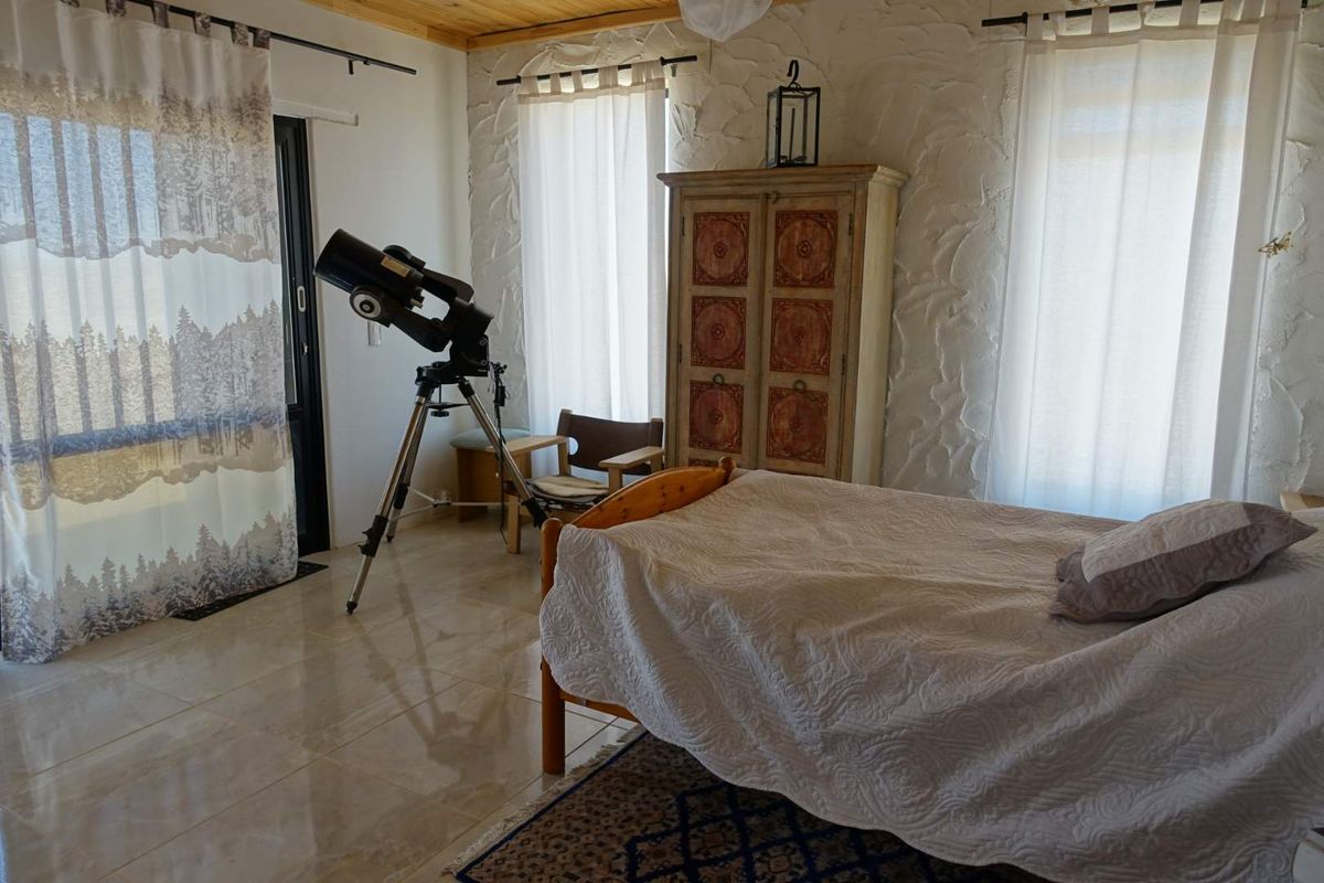 A bedroom featuring textured white walls, tiled flooring, and a wooden ceiling, with access to an outdoor area through a sliding glass door.