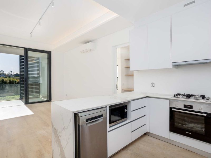 Modern open-plan kitchen featuring high-end stone countertops, integrated appliances, and seamless flow to a private balcony through large sliding glass doors.