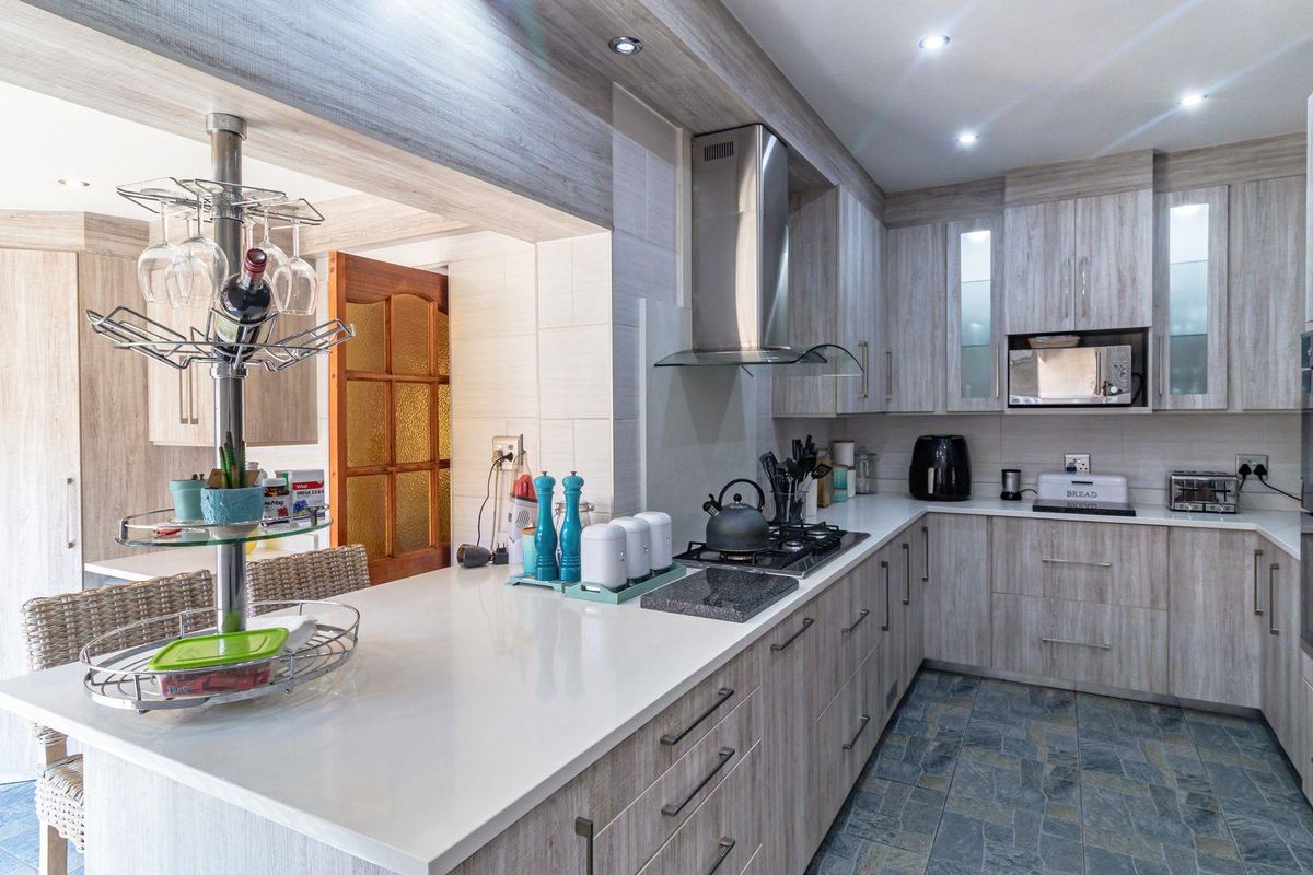 Modern kitchen featuring light wood-grain cabinetry, stone countertops, integrated appliances, and stone tile flooring with a breakfast bar peninsula.