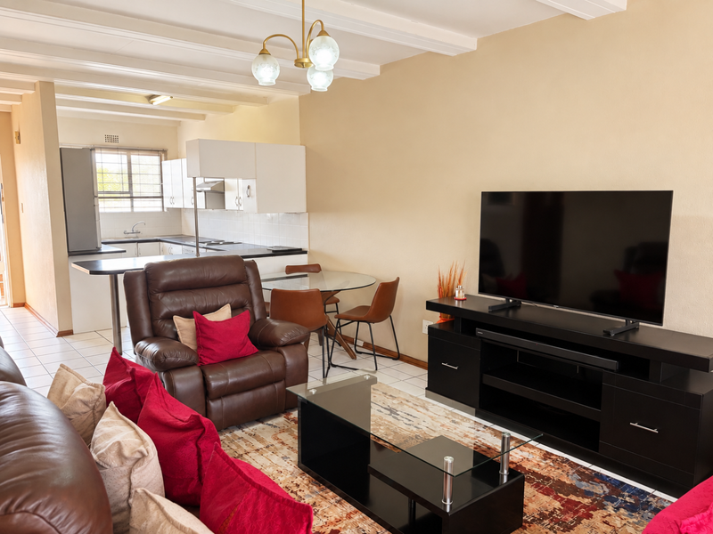 Open-plan living and kitchen area featuring tiled floors, exposed ceiling beams, and a functional kitchen layout with a breakfast bar.