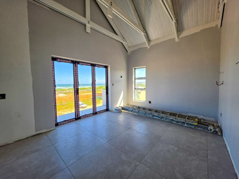 An unfinished living area featuring vaulted ceilings with exposed rafters, large stacker doors opening to a coastal view, and modern floor tiling.