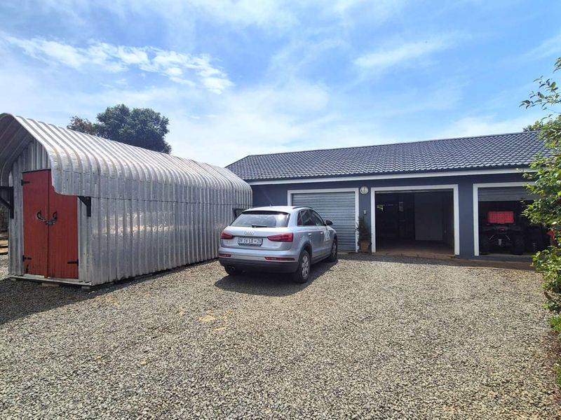 Exterior view of a small holding featuring a triple garage with a tiled roof and a separate corrugated metal storage shed on a gravel driveway.