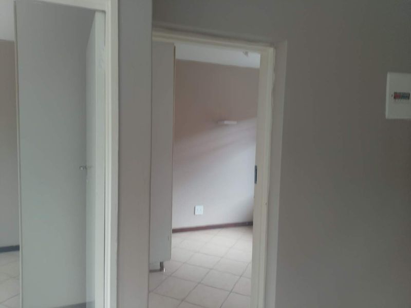 A view through a hallway into an adjacent room, featuring tiled flooring and a wall-mounted electrical distribution board.