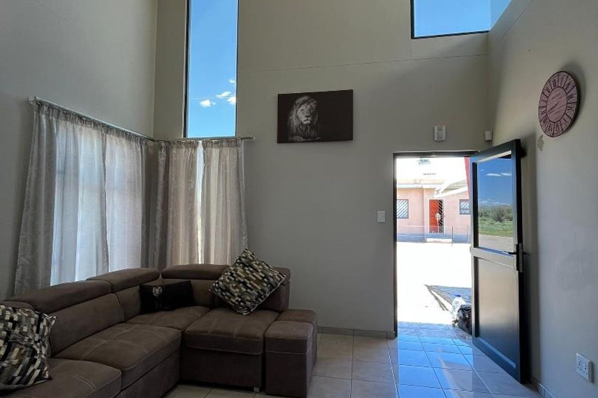 Spacious living area featuring high vaulted ceilings, large vertical windows for natural light, and tiled flooring with direct access to the exterior.