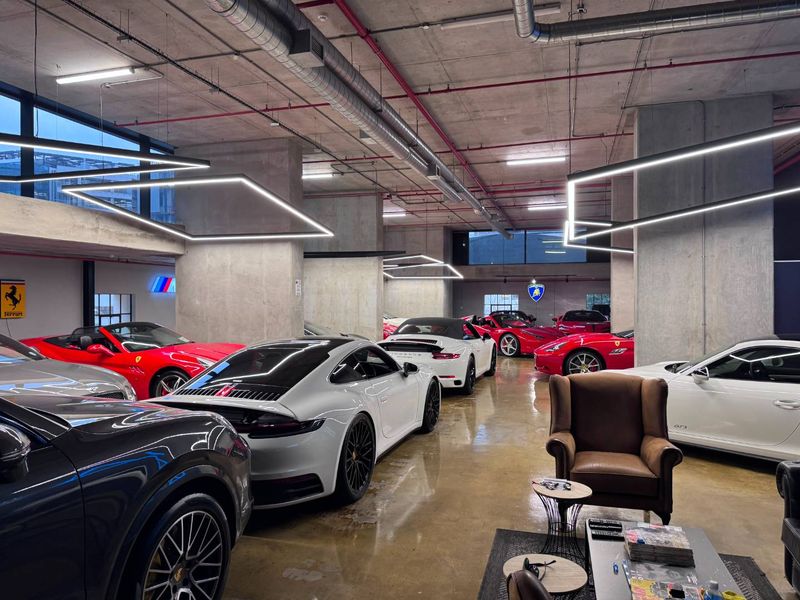 Spacious industrial-style garage featuring exposed concrete ceilings, polished concrete floors, and modern linear lighting, designed for high-end vehicle storage.