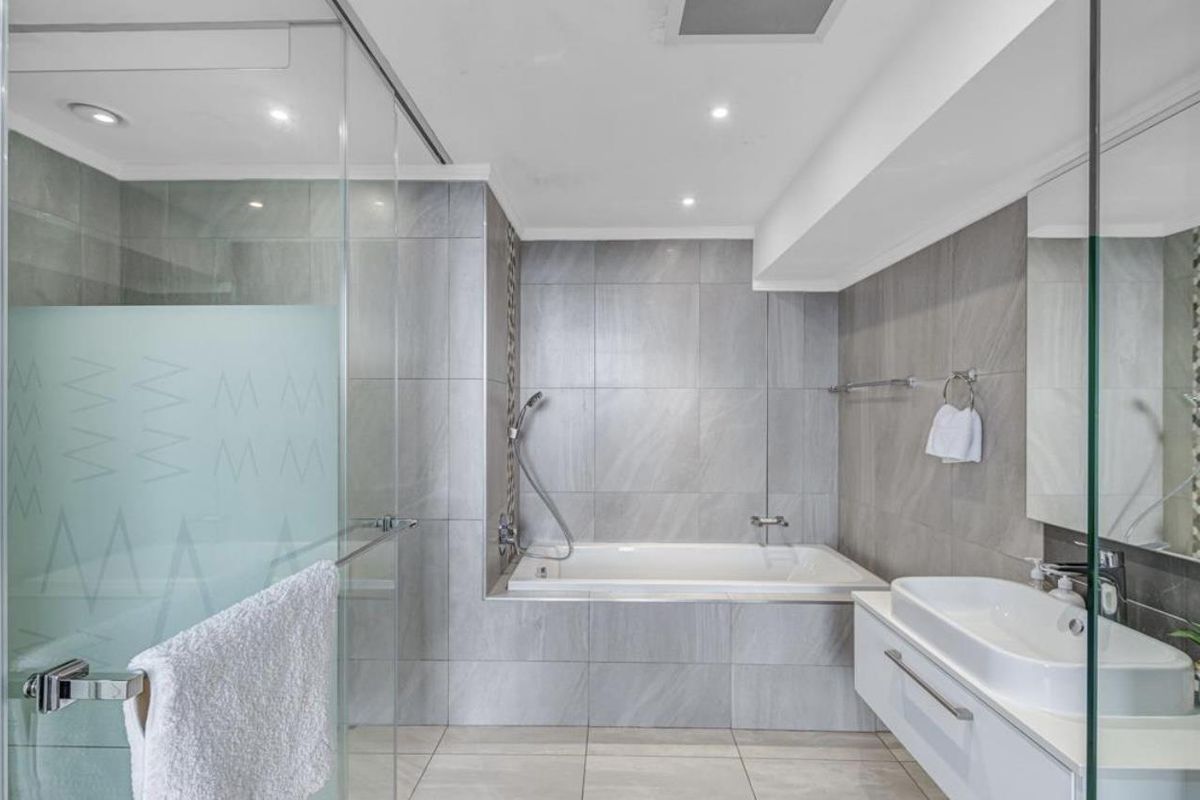 Modern bathroom featuring a built-in bathtub, glass-enclosed shower, and a wall-mounted vanity with a basin, finished with contemporary grey tiling.