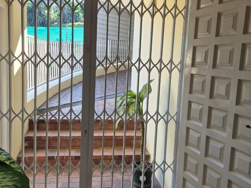 Entrance area featuring a white panelled door and a metal security gate leading to external brick steps.