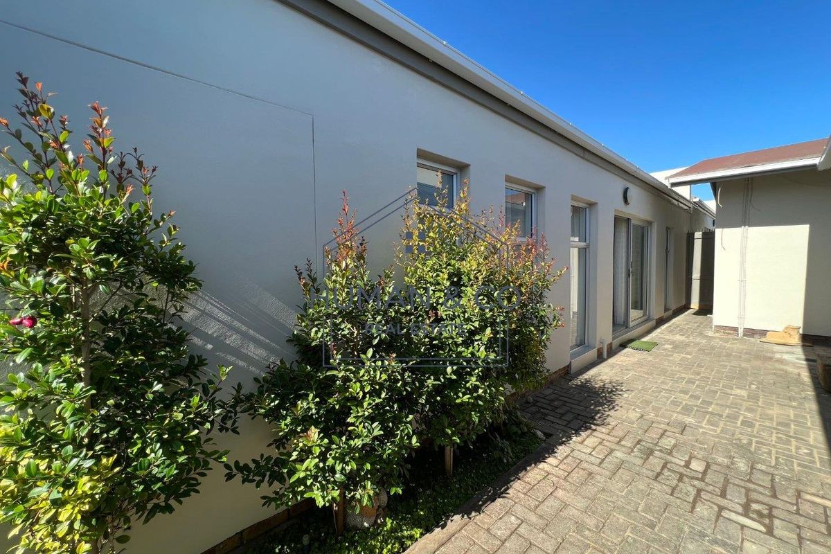 A well-maintained rear exterior view featuring a paved courtyard, clean rendered walls, and modern aluminium sliding doors and window frames.