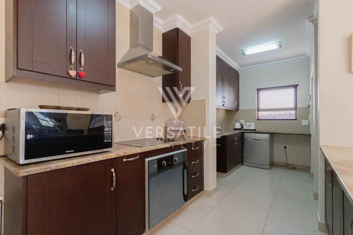 A functional kitchen featuring dark wood cabinetry, granite countertops, a built-in oven, stainless steel extractor fan, and tiled flooring.