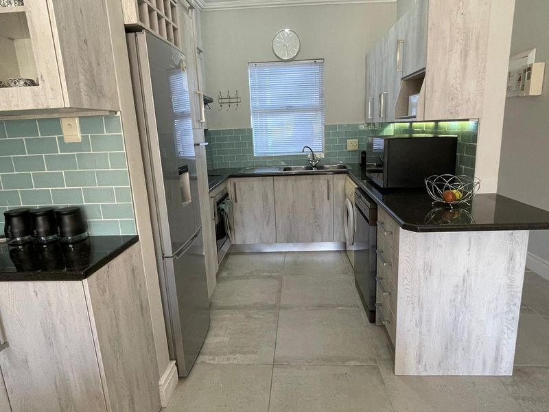 Modern kitchen featuring light wood-grain cabinetry, black granite countertops, a stylish teal subway tile backsplash, and integrated under-cabinet lighting.