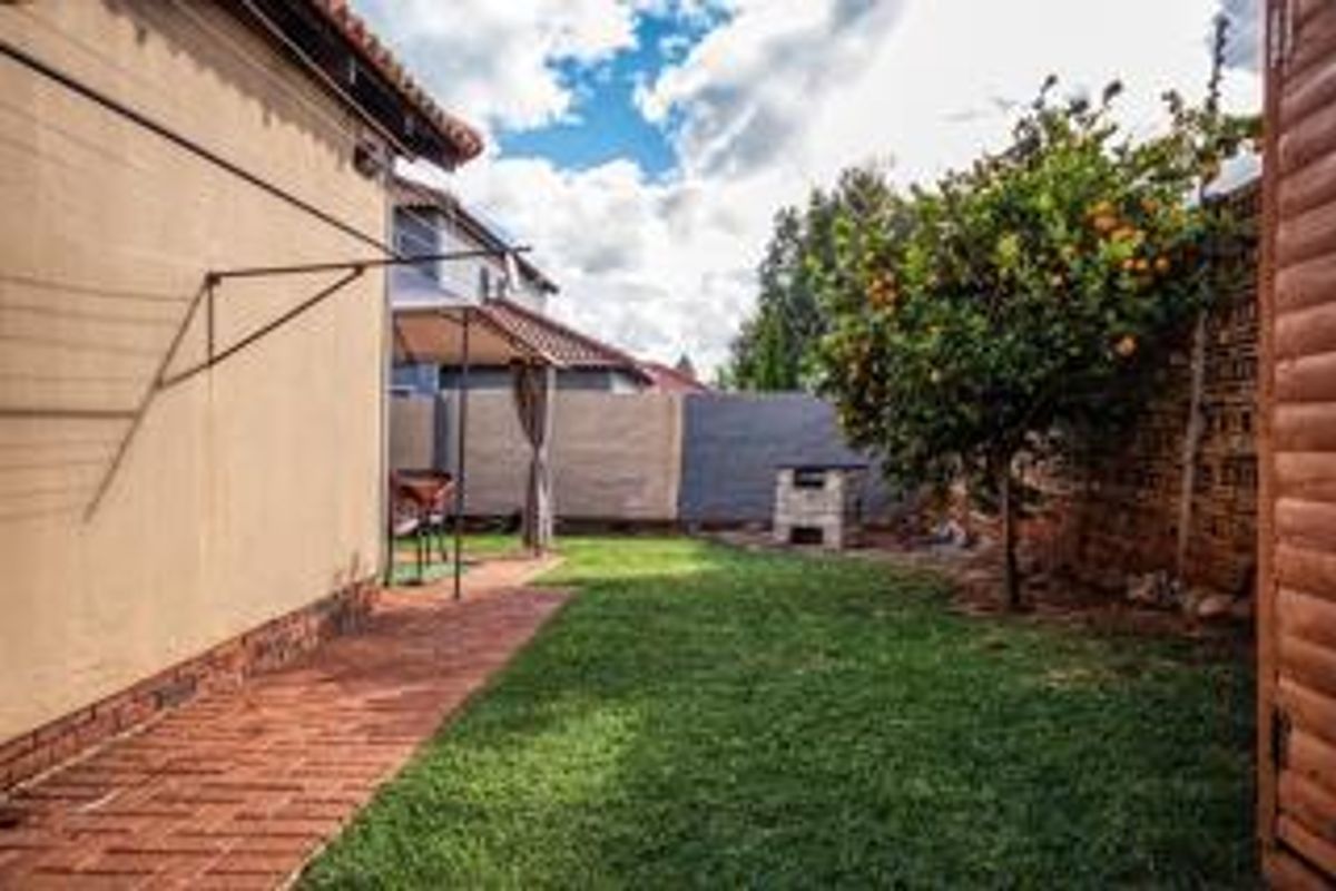 A private rear garden featuring a brick-paved walkway, a small lawn area, a built-in braai, and a wall-mounted washing line.