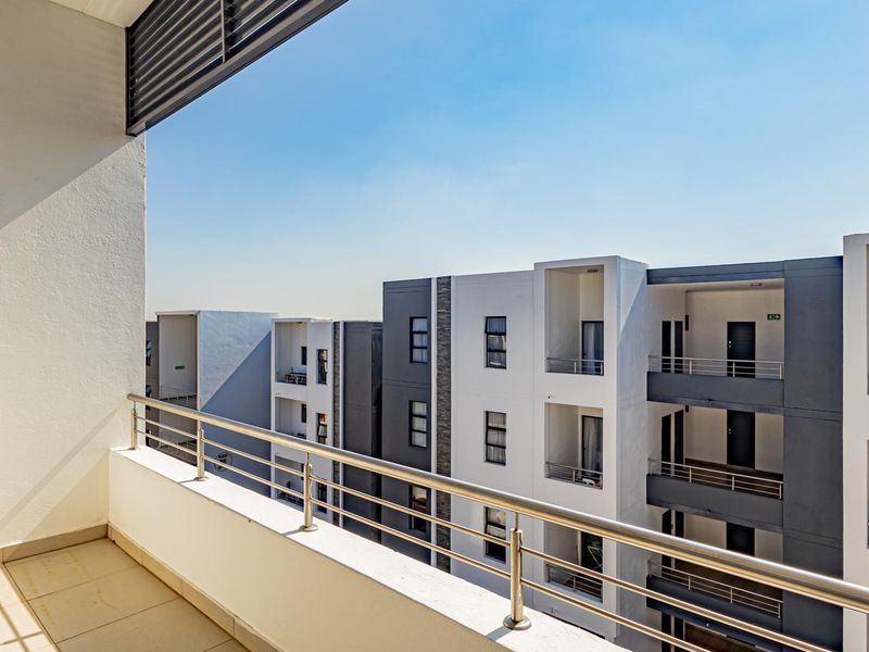 A modern, well-maintained balcony featuring tiled flooring and a stainless steel balustrade, offering an elevated view of the surrounding apartment complex.