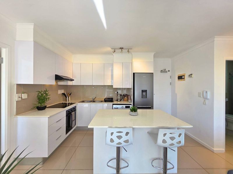 Modern kitchen featuring white high-gloss cabinetry, stone countertops, a central island with breakfast bar seating, and integrated appliances.
