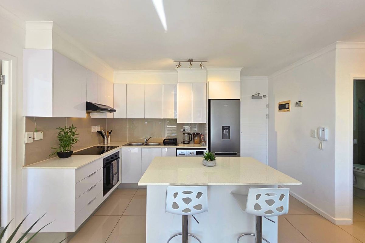Modern kitchen featuring white high-gloss cabinetry, stone countertops, a central island with breakfast bar seating, and integrated appliances.