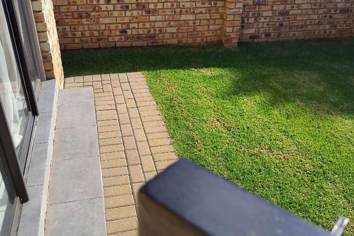 A private rear garden featuring a paved patio area, well-maintained lawn, and a secure face brick boundary wall.