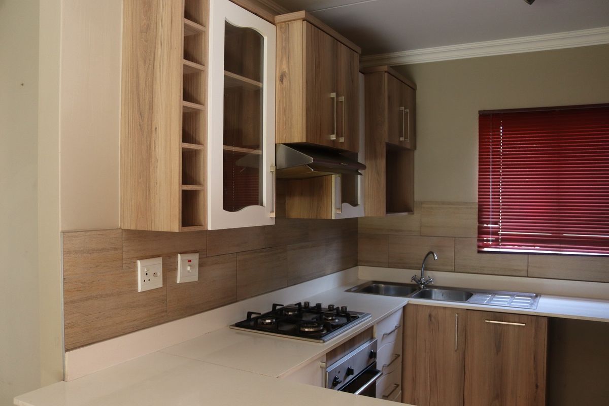 A well-maintained kitchen featuring wood-finish cabinetry, a gas hob, built-in oven, extractor fan, and a double sink with a tiled backsplash.