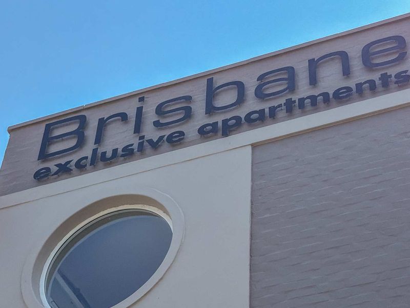 Exterior view of the Brisbane Exclusive Apartments building facade featuring prominent signage and a circular window design.