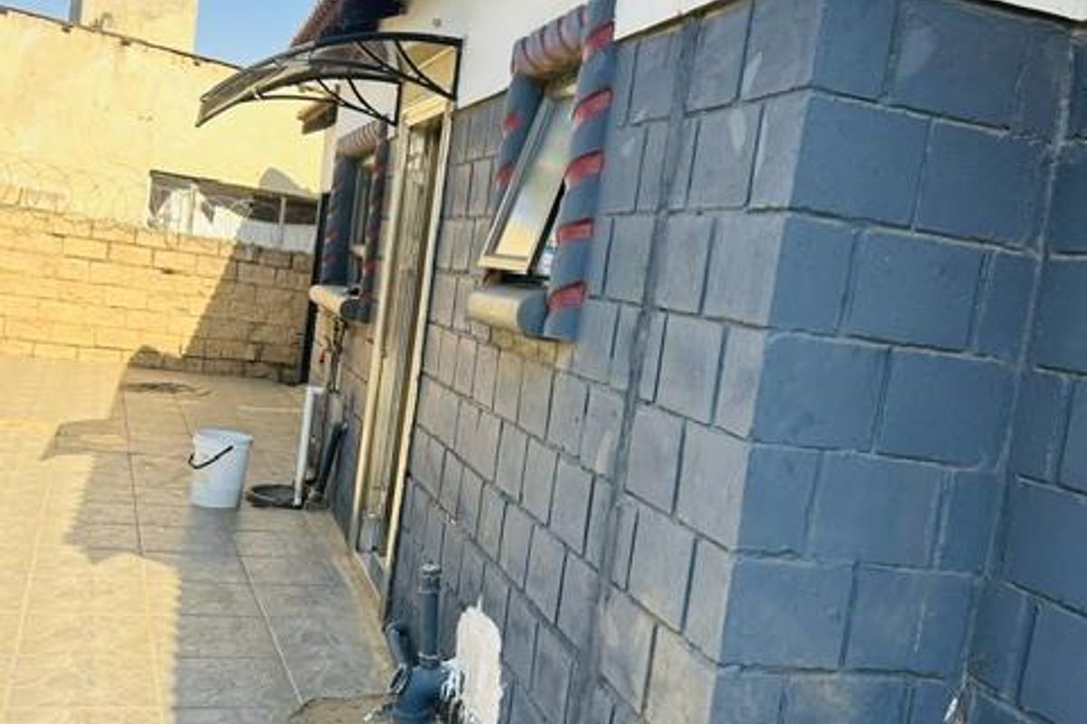 Rear exterior view of the property featuring a paved patio area, exposed brickwork, and external plumbing fixtures.