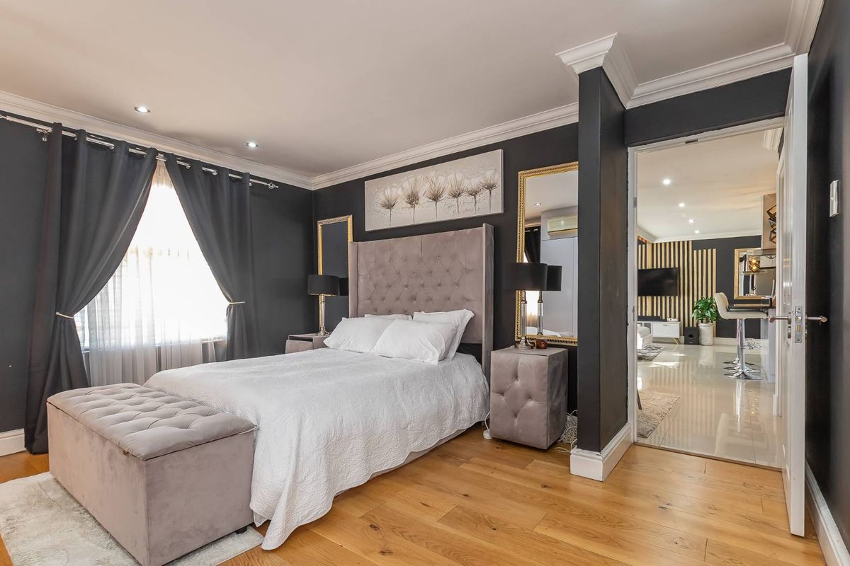 A well-appointed bedroom featuring hardwood flooring, crown molding, and recessed lighting, with an open doorway leading to an adjacent living area.