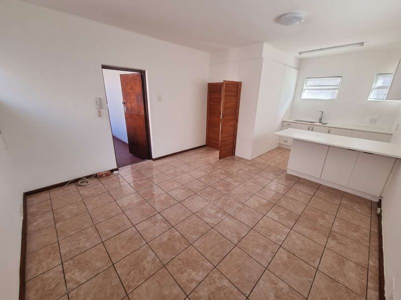 Open-plan living and kitchen area featuring tiled flooring, built-in cabinetry, a breakfast counter, and neutral walls, offering a blank canvas for personalization.