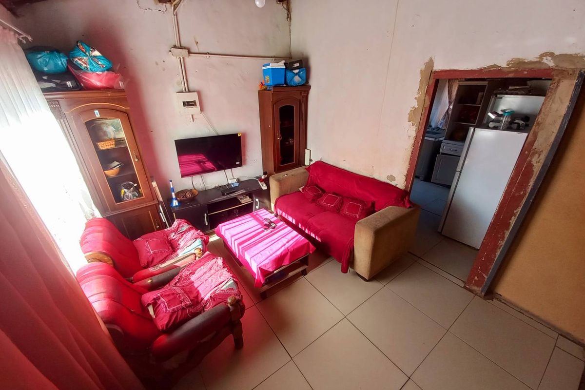 A living room area featuring tiled flooring and direct access to an adjacent kitchen space, requiring cosmetic updates and wall repairs.