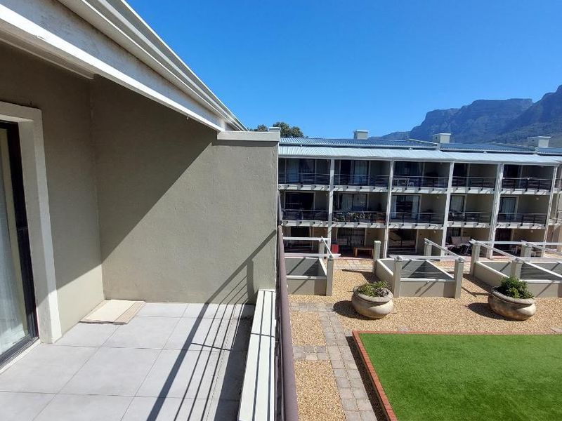 A spacious balcony with tiled flooring and metal railings, offering an elevated view of the complex courtyard and surrounding mountain landscape.