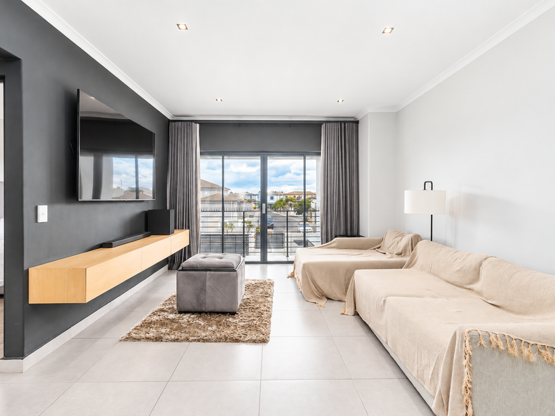 Modern living room featuring tiled floors, a sleek floating timber media console, and large sliding glass doors leading to a balcony with neighborhood views.