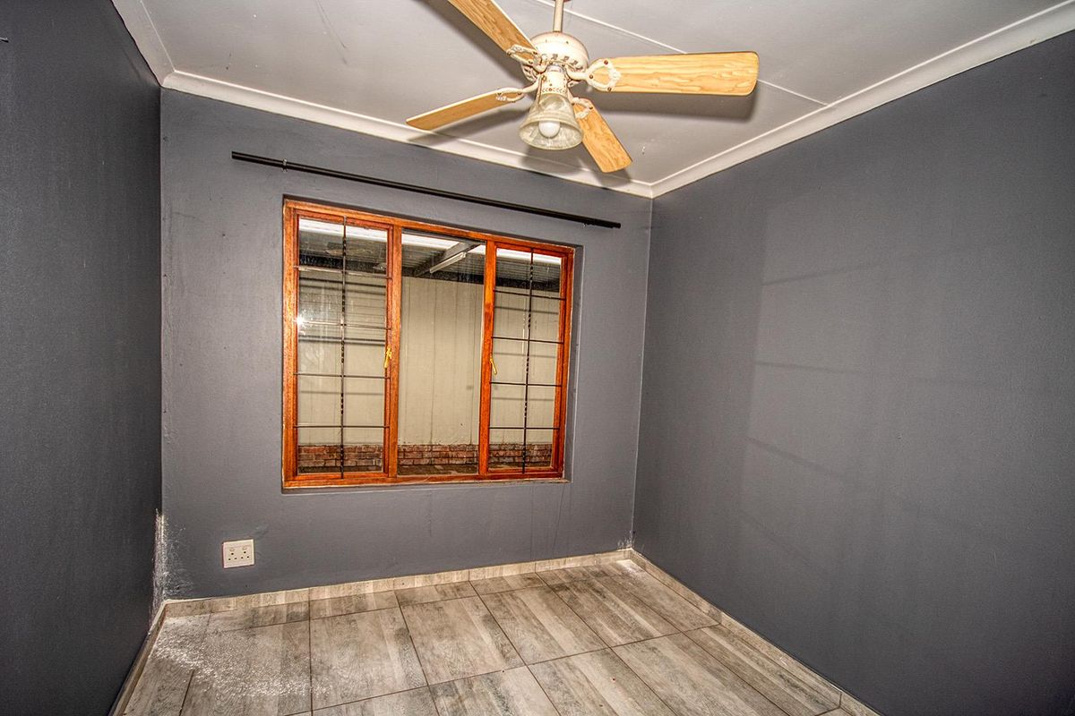 A compact bedroom featuring dark grey walls, wood-framed window with security bars, tiled flooring, and a ceiling fan.
