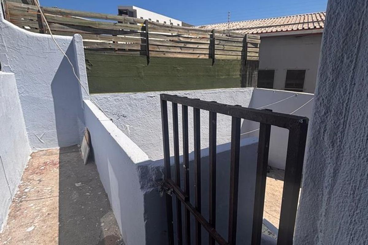 A small, enclosed outdoor utility area featuring concrete flooring, painted boundary walls, and a metal security gate.